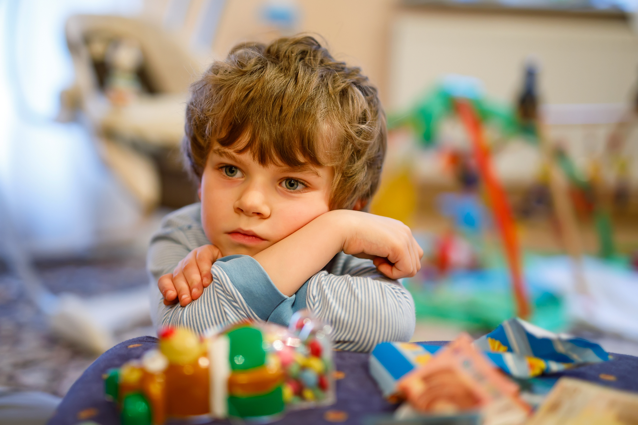 Portrait of little kid boy sad on birthday. child with lots of toys. Tired preschool boy